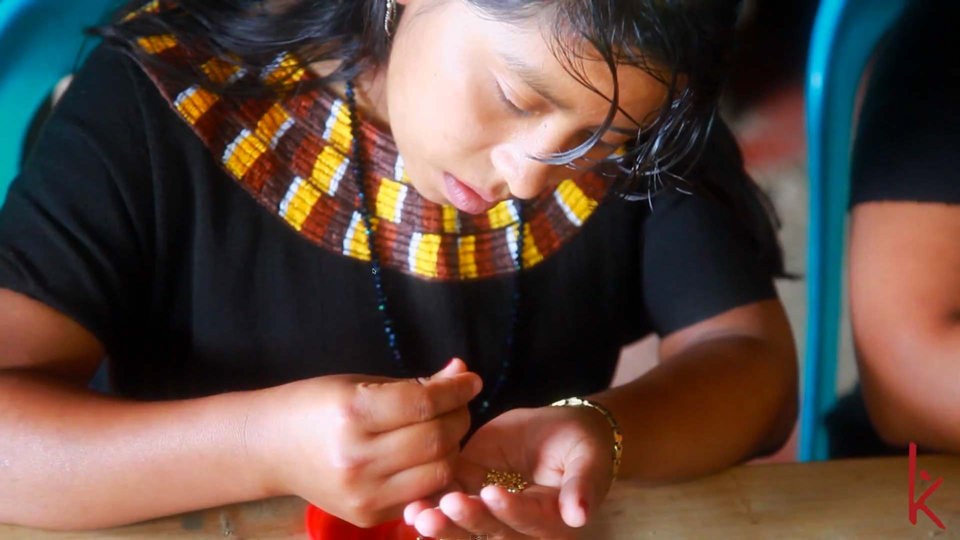 Stillbild ur filmen Wakami - Our Roots: en kvinna arbetar med pärlor till ett smycke